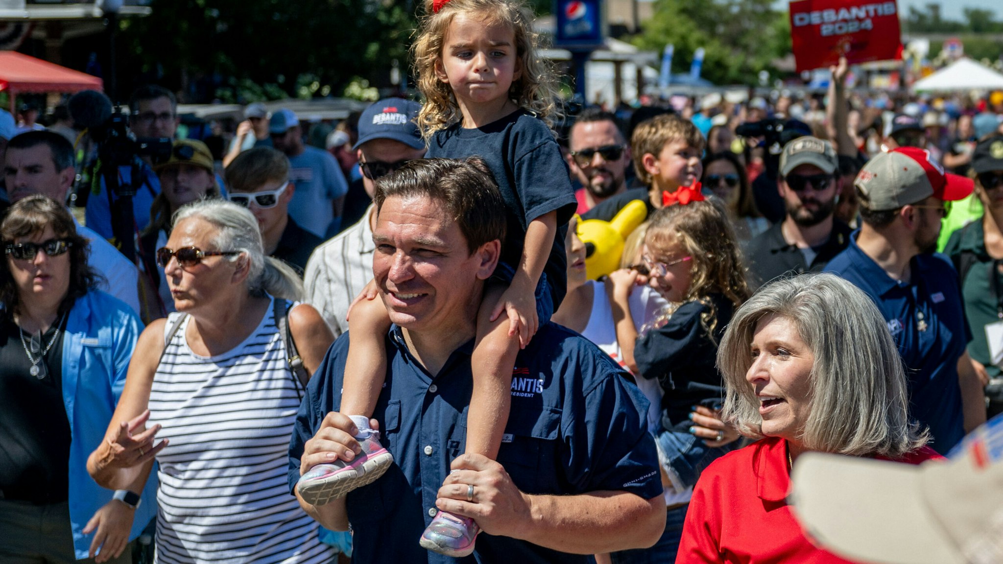 DES MOINES, IOWA - AUGUST 12: Republican presidential candidate Florida Gov. Ron DeSantis carries his daughter Madison while walking alongside Sen. Joni Ernst (R-IA) through the Iowa State Fair on August 12, 2023 in Des Moines, Iowa. Republican and Democratic presidential hopefuls, including Florida Gov. Ron DeSantis, former President Donald Trump are visiting the fair, a tradition in one of the first states to hold caucuses in 2024.