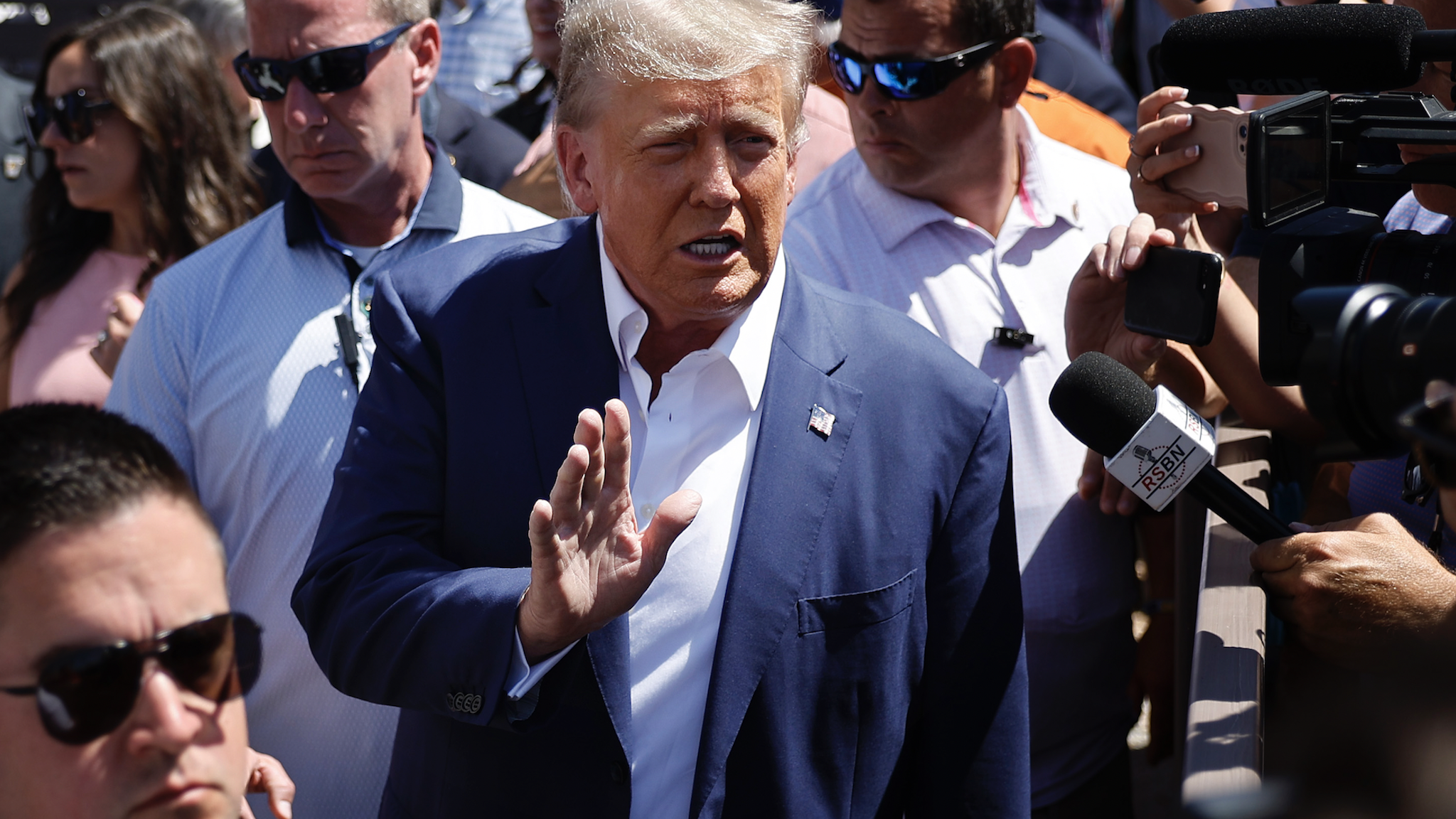DES MOINES, IOWA - AUGUST 12: Surrounded by campaign staff and members of the U.S. Secret Service, Former U.S. President Donald Trump (C) waves to supporters as he visits the Iowa Pork Producers Tent at the Iowa State Fair on August 12, 2023 in Des Moines, Iowa. Republican and Democratic presidential hopefuls are visiting the fair, a tradition in one of the first states that will test candidates with the 2024 caucuses.