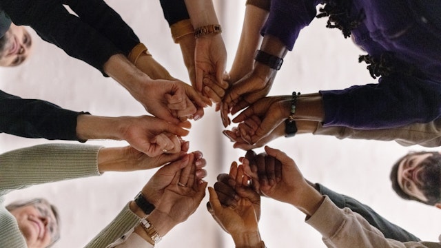 Low angle view of group of people in circle and holding their fists together during a group therapy session. People with fist put together during support group session.