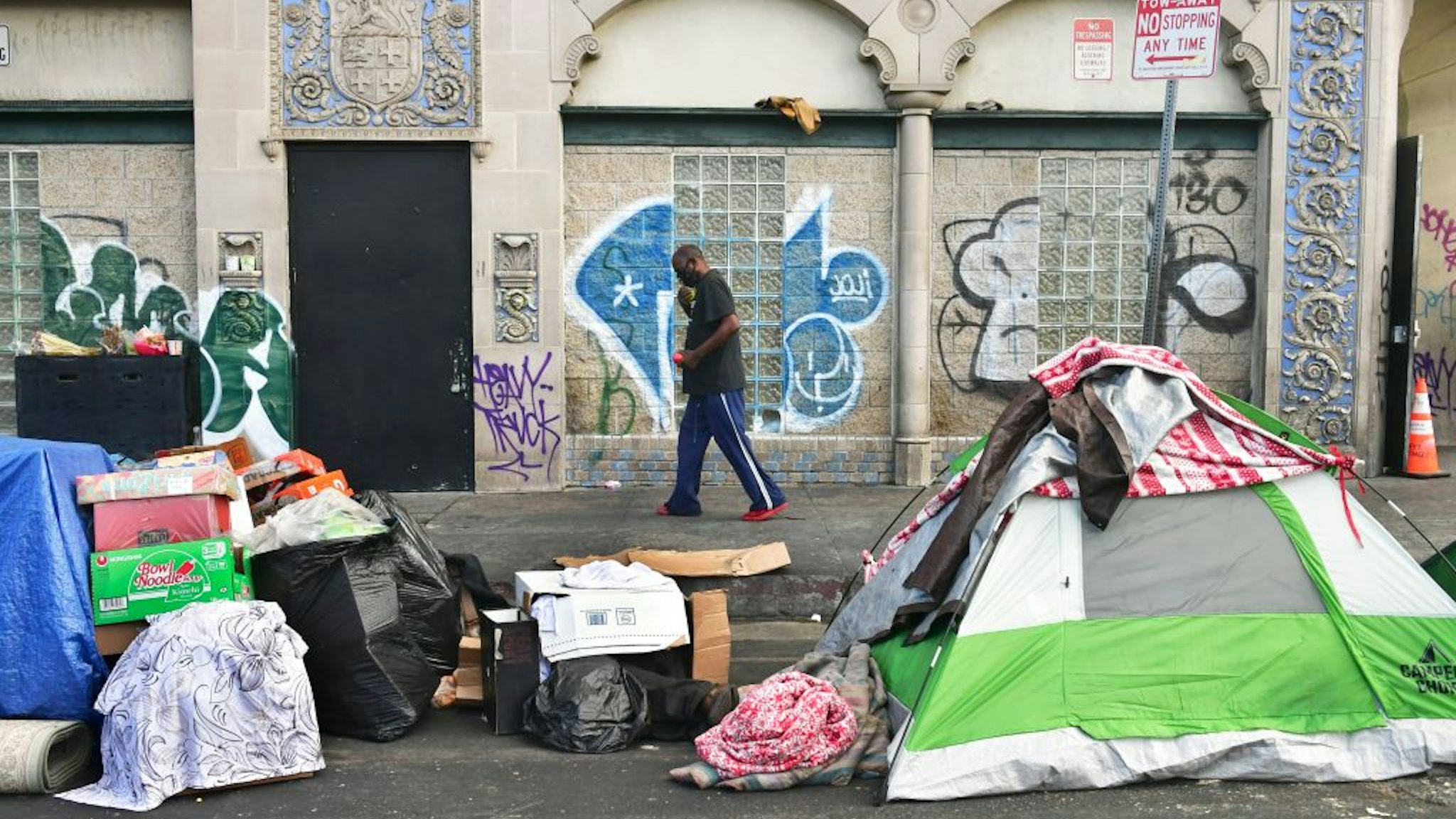 A man walks past tents housing the homeless on the streets in the Skid Row community of Los Angeles, California on April 26, 2021. - A federal judge overseeing a lawsuit that seeks to end the city's Skid Row homelessness crisis isn't backing down from his order requiring that all indigent persons in the area be offered shelter within six months. US District Judge David O. Carter is opening the door for more discussions by setting additional hearing dates and clarifying some portions of his ruling. (Photo by Frederic J. BROWN / AFP) (Photo by FREDERIC J. BROWN/AFP via Getty Images)