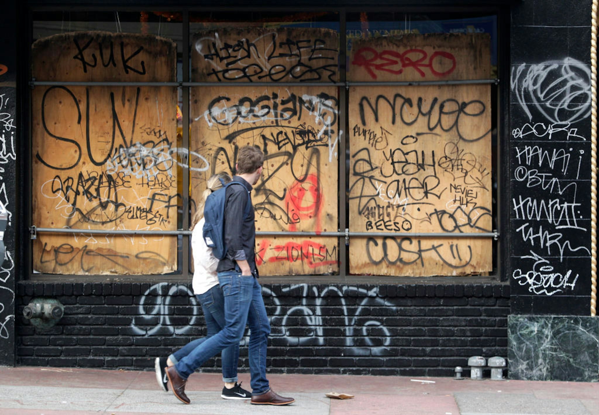 Pedestrians walk past a graffiti covered storefront on Mission Street in San Francisco, Calif. on Thursday, Oct. 30, 2014 after the Giants beat the Kansas City Royals in the World Series. The celebration turned ugly when crowds became unruly and vandalized several businesses and vehicles. (Photo By Paul Chinn/The San Francisco Chronicle via Getty Images)