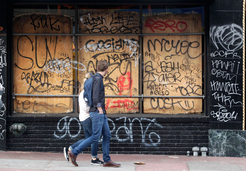 Pedestrians walk past a graffiti covered storefront on Mission Street in San Francisco, Calif. on Thursday, Oct. 30, 2014 after the Giants beat the Kansas City Royals in the World Series. The celebration turned ugly when crowds became unruly and vandalized several businesses and vehicles. (Photo By Paul Chinn/The San Francisco Chronicle via Getty Images)