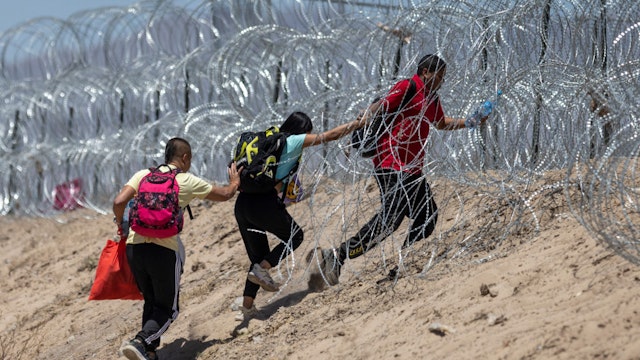 EL PASO, TEXAS - MAY 11: Immigrants walk through razor wire surrounding a makeshift migrant camp after crossing the border from Mexico on May 11, 2023 in El Paso, Texas. The number of immigrants reaching the border has surged with the end of the U.S. government's Covid-era Title 42 policy, which for the past three years has allowed for the quick expulsion of irregular migrants entering the country.