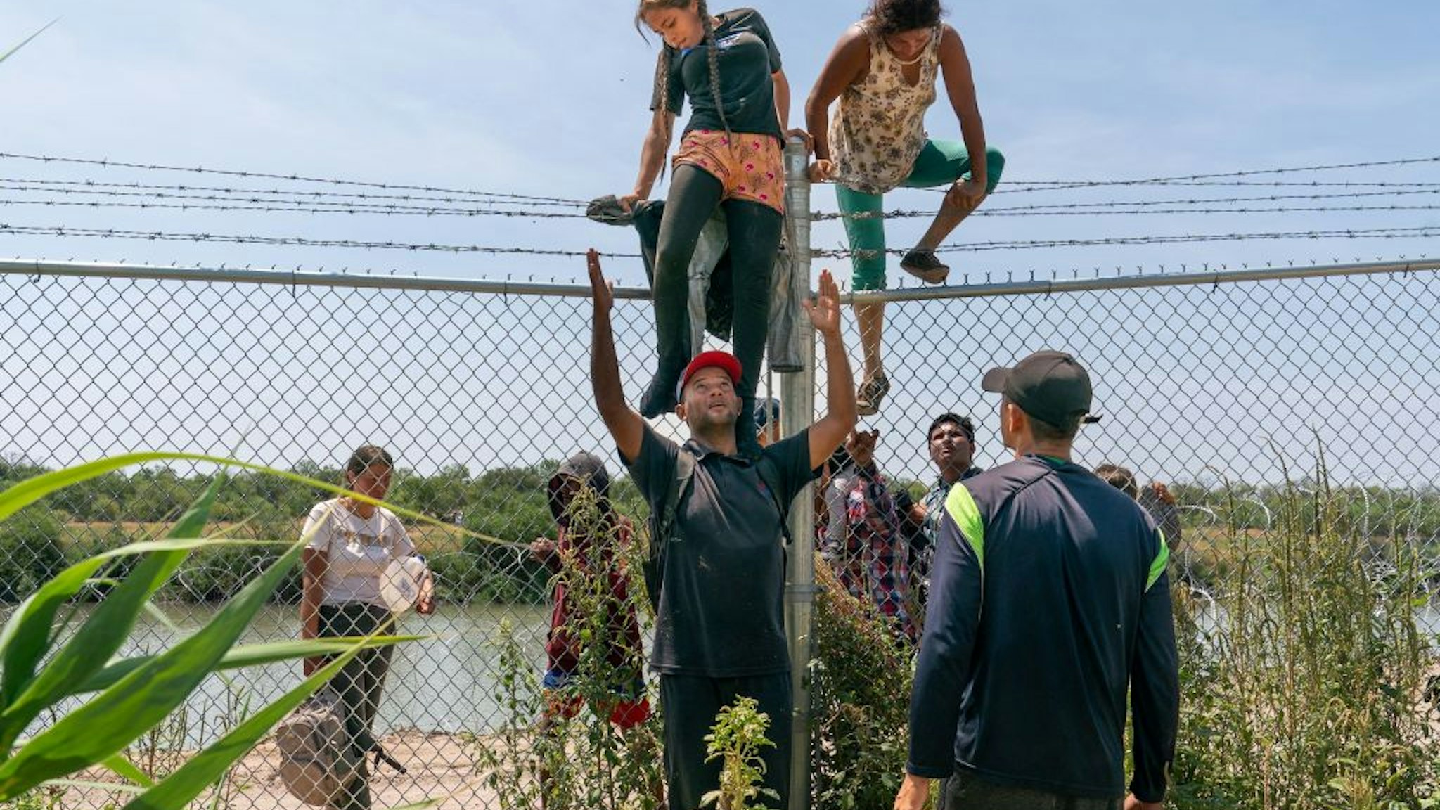 TOPSHOT - Migrants help each other climb over a barbed wire fence into the US from Mexico, in Eagle Pass, Texas, on August 25, 2023. With their two children on their shoulders, Wilfredo and Nataly jump into the Rio Grande from the Mexican shore. The water is up to their waists. They avoid the line of buoys that the state of Texas placed to block their passage and head for the United States. They cross from Piedras Negras, Coahuila state, and seek the opposite bank in Eagle Pass, a city in southern Texas whose governor, Republican Greg Abbott, has militarized the river to contain the entry of migrants. (Photo by SUZANNE CORDEIRO / AFP) (Photo by SUZANNE CORDEIRO/AFP via Getty Images)