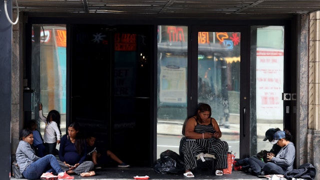 Venezuelan migrants sit on the sidewalk outside the Inn of Chicago on Aug. 17, 2023. (Antonio Perez/Chicago Tribune/Tribune News Service via Getty Images)