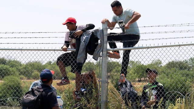 Migrants jump over the barbed wire fence in Rio Grande in Eagle Pass, Texas after crossing into US from Mexico on August 25, 2023. (Photo by SUZANNE CORDEIRO / AFP) (Photo by SUZANNE CORDEIRO/AFP via Getty Images)