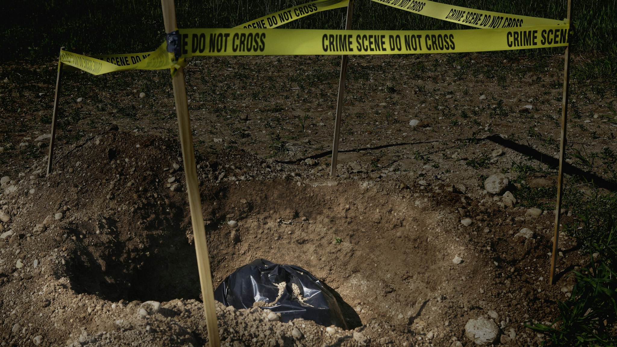 Garbage bag in dug hole with crime scene tape - stock photo