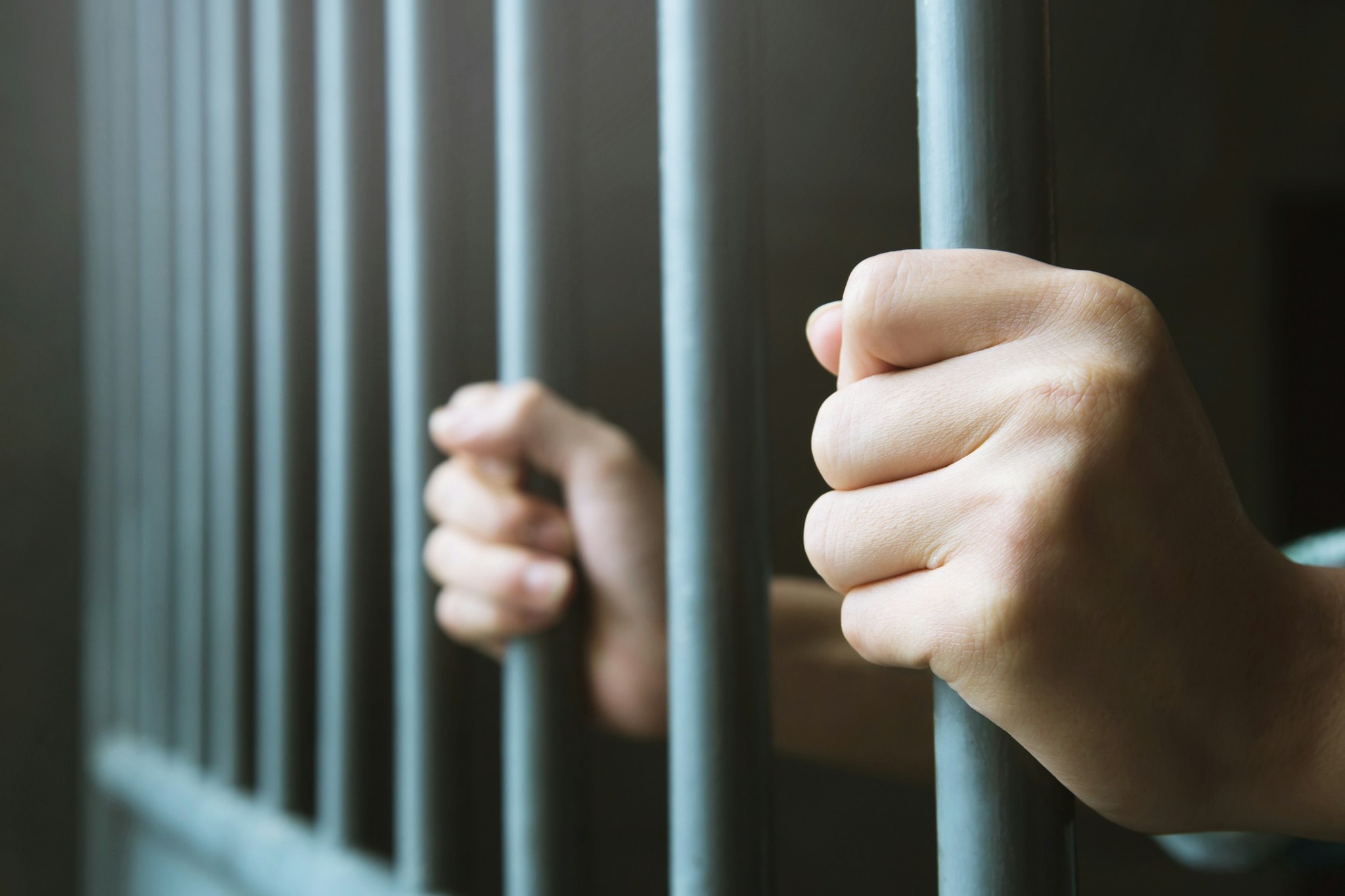 Man in prison hands of behind hold Steel cage jail bars. offender criminal locked in jail. - stock photo