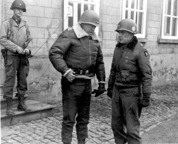 American military commander Lieutenant General George S. Patton (1885 - 1945) (center left) talks with Brigadier General Anthony McAuliffe (1898 - 1975), Bastogne, France, December 28, 1944. McAuliff commanded the 101st Airborne Division, which was beseiged in Bastogne during the Battle of the Bulge, until the seige was broken by troops under Patton shortly before this picture was taken. (Photo by PhotoQuest/Getty Images)