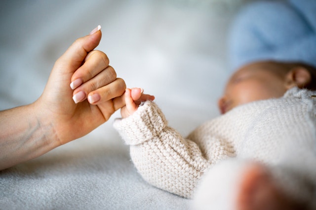 Close-up of mother's hand holding newborn baby's hand. StockPlanets. Getty Images.