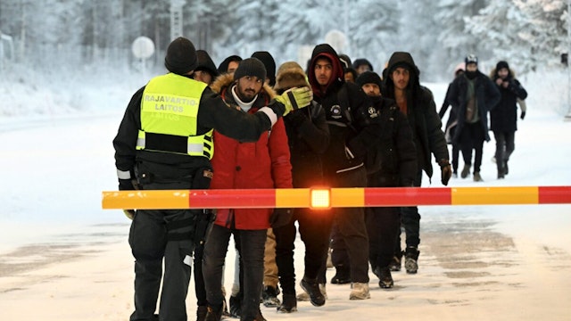 A Finnish Border Guard speaks to migrants at the international border crossing at Salla, northern Finland, on November 23, 2023. Russia announced tightened security in its northern Murmansk region after Finland said it would close all but one border crossing between the two countries. Helsinki said on November 22, 2023 the move follows a surge in attempted crossings by migrants seeking asylum in the EU country -- which Finland says is a destabilisation ploy by Russia.