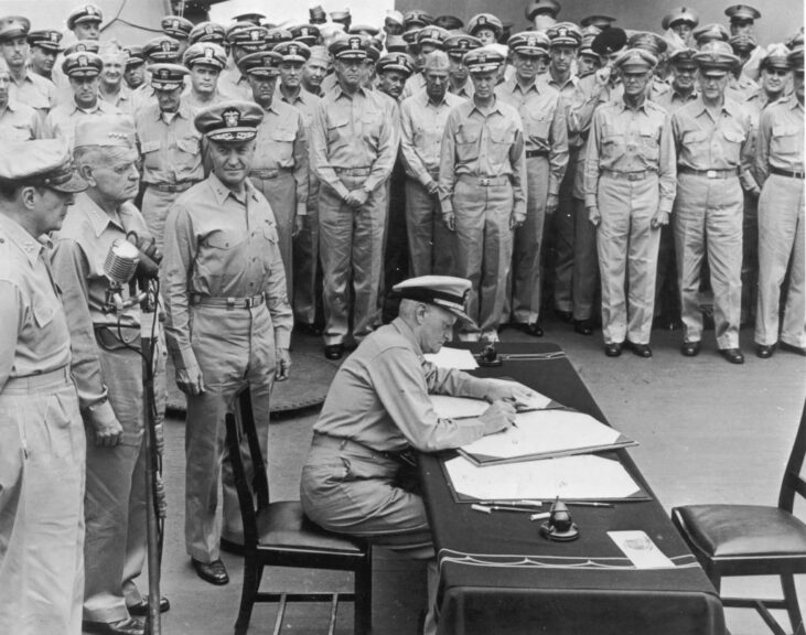2nd September 1945: US Fleet Admiral Chester W. Nimitz signs surrender documents recognizing the defeat of Japan as officials and soldiers look on, USS Missouri, Tokyo Bay, Japan, World War II. General Douglas MacArthur (left), Admiral William F. Halsey (centre), and Rear Admiral Forrest P. Sherman stand behind Nimitz. (Photo by Hulton Archive/Getty Images)