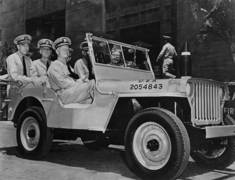 Admiral Chester William Nimitz (1885 - 1966, centre), the Commander-in-Chief of the US Pacific Fleet, takes a ride around Pearl Harbor in Hawaii with his aides-de-camp, in a jeep presented to the fleet by the Hawaiian department of the US Army in honour of their naval victory at Midway Island, January 1942. The former army jeep is painted battleship grey. From left to right, Commander R. F. Good of the US Navy, Rear Admiral Milo F. Draemel of the US Navy, Admiral Nimitz, Captain Walter S. Delany of the US Navy and Colonel Morrill W. Marston of the US Army. (Photo by Three Lions/Hulton Archive/Getty Images)