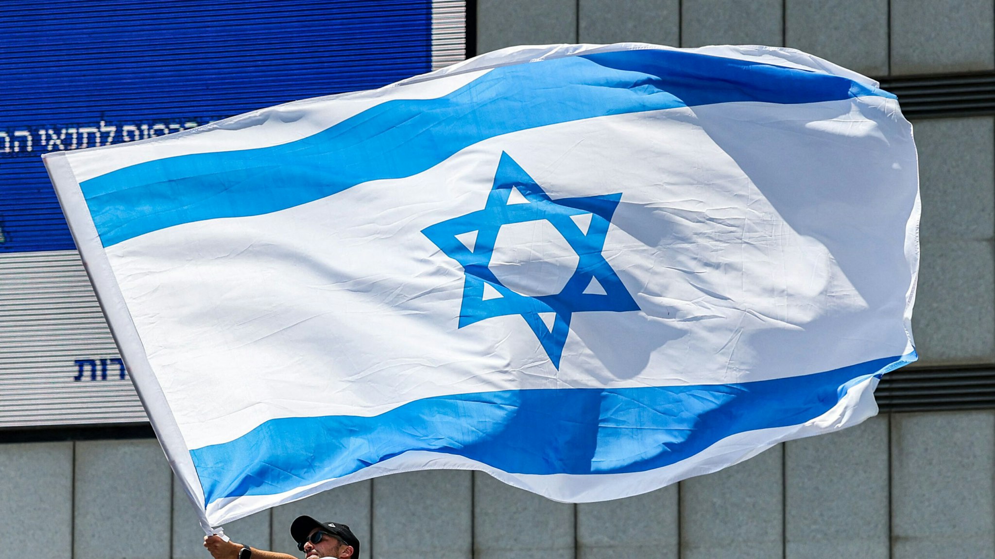 A man waves a large Israeli flag as anti-government demonstrators rally during a protest in Tel Aviv on July 11, 2023. Protesters blocked roads across Israel on July 11 hours after parliament adopted in a first reading a key clause of the government's judicial overhaul package which opponents say threatens democracy.