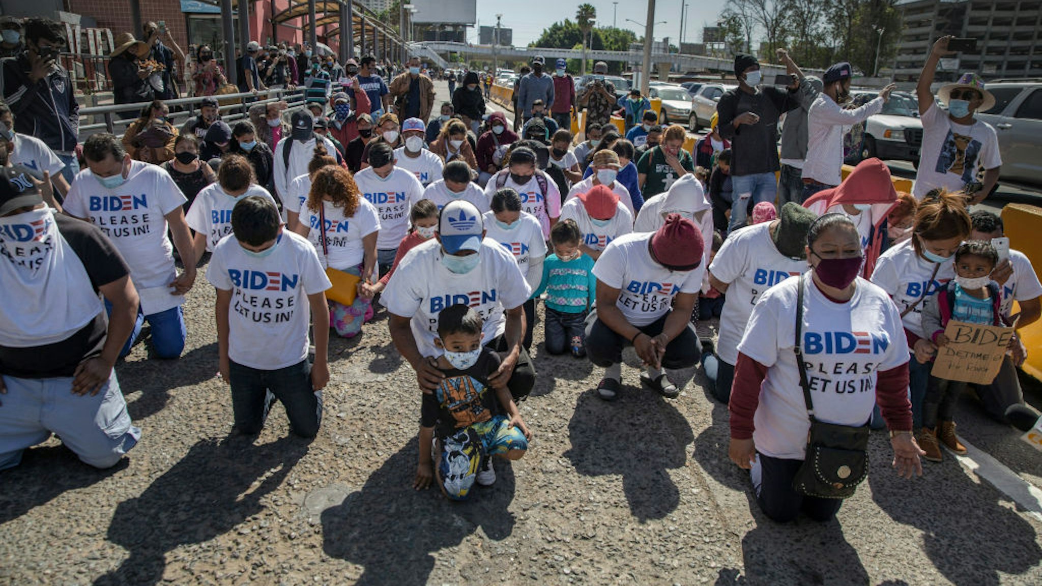02 March 2021, Mexico, San Ysidro: A group of migrants wearing T-shirts that read "Biden, please let us in" kneel and pray at the border crossing. The group gathered and marched up to the border post to petition the new U.S. administration for asylum. U.S. Border Patrol (CPB) agents conducted a heavier operation at the border crossing with the goal of preventing a stampede.