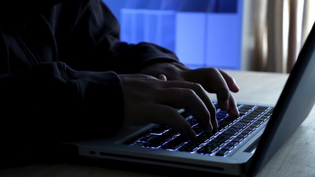 Hacker working on laptop at night under blue light.