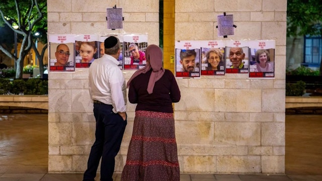 10/30/2023, Jerusalem, Israel. Religious Israelis look at posters of hostages from Kibbutz Nir-Oz near a hostages in the Jerusalem Municipality Square. The display was put on by survivors of Kibbutz Nir-Oz for the return of the abductees. The beds are meant to remind that the hostages were kidnapped from their beds, and others were murdered in them. 239 hostages are currently being held by Hamas. (Photo by Yahel Gazit / Middle East Images / Middle East Images via AFP) (Photo by YAHEL GAZIT/Middle East Images/AFP via Getty Images)