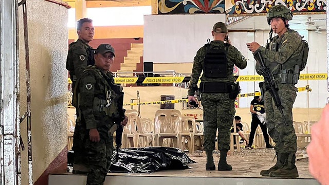 Military personnel stand guard at the entrance of a gymnasium while police investigators (background) look for evidence after a bomb attack at Mindanao State University in Marawi, Lanao del sur province on December 3, 2023. At least three people were killed and seven wounded in a bomb attack on a Catholic mass in the insurgency-plagued southern Philippines on December 3, officials said.