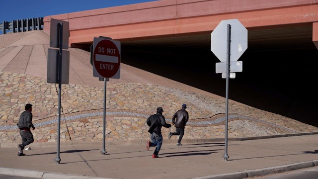 TOPSHOT - Migrants run into the street to evade law enforcement after illegally crossing into the US via a hole in a fence in El Paso, Texas, on December 22, 2022. - The US Supreme Court halted December 19, 2022 the imminent scrapping of a key policy used since Donald Trump's administration to block migrants at the southwest border, amid worries over a surge in undocumented immigrants. An order signed by Chief Justice John Roberts placed an emergency stay on the removal planned for December 21, 2022 of Title 42, which allowed the government to use Covid-19 safety protocols to summarily block the entry of millions of migrants. (Photo by Allison Dinner / AFP) (Photo by ALLISON DINNER/AFP via Getty Images)