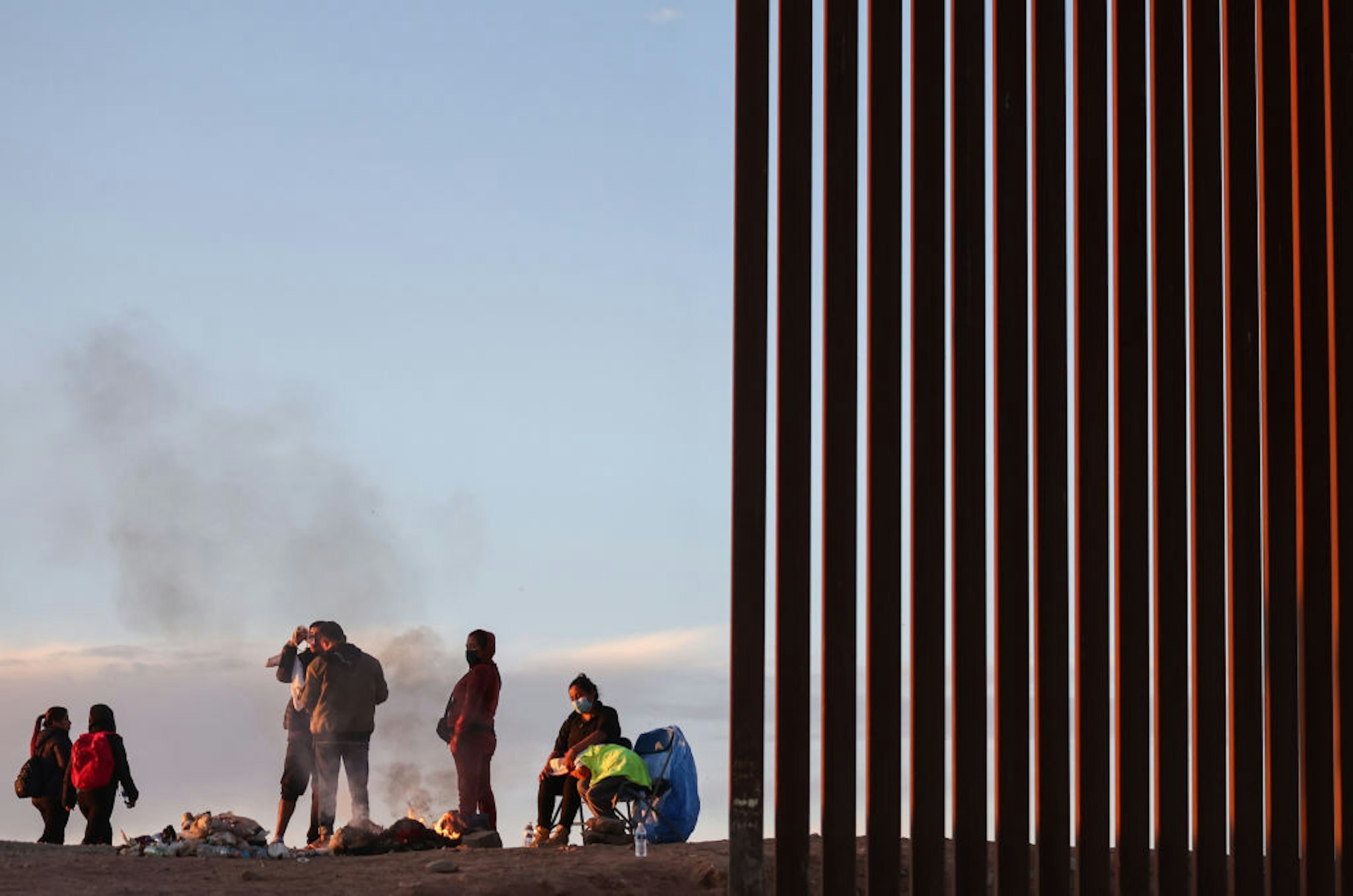 YUMA, ARIZONA - MAY 22: Immigrants from Ecuador warm themselves by a fire after sunrise along a gap in the U.S.-Mexico border barrier, as they await processing by the U.S. Border Patrol, after crossing from Mexico on May 22, 2022 in Yuma, Arizona. Title 42, the controversial pandemic-era border policy enacted by former President Trump, which cites COVID-19 as the reason to rapidly expel asylum seekers at the U.S. border, was set to officially expire on May 23rd. A federal judge in Louisiana delivered a ruling May 20th blocking the Biden administration from lifting Title 42. (Photo by Mario Tama/Getty Images)
