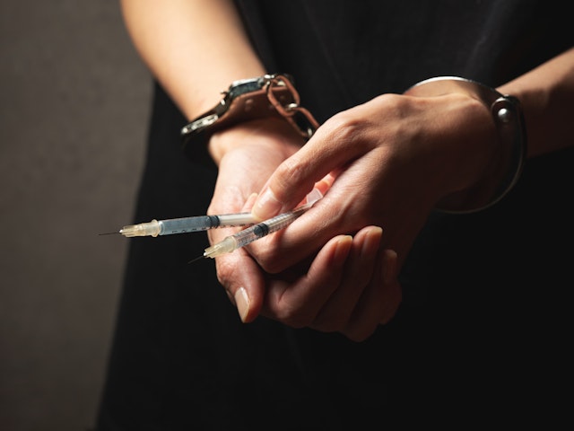 Handcuffs on wrist, drug syringe