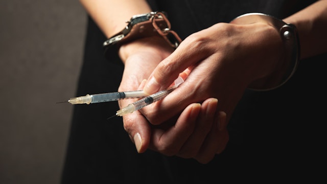 Handcuffs on wrist, drug syringe