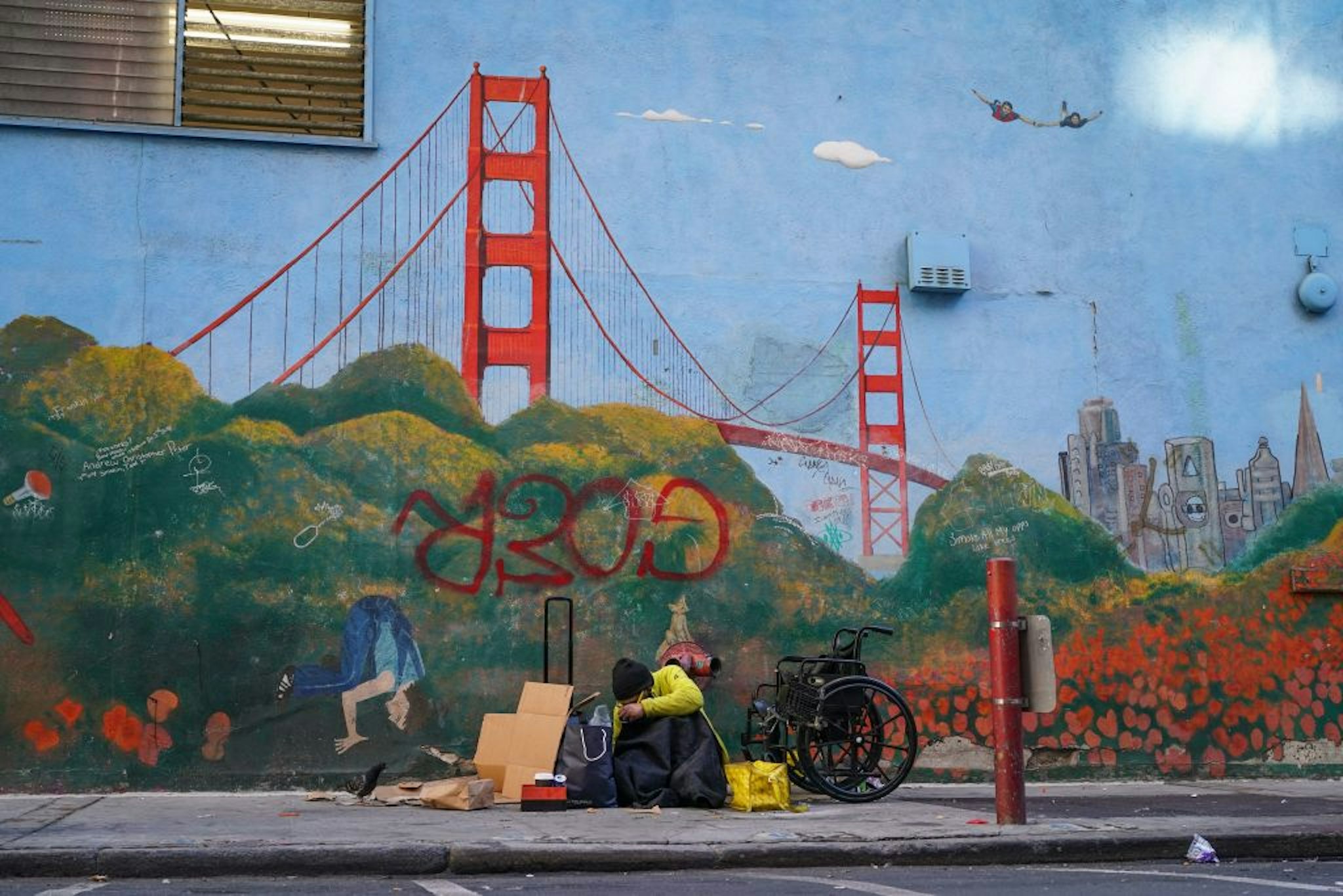 A homeless person lies against a mural of the Golden Gate Bridge near APEC Summit headquarters on November 11, 2023 in downtown San Francisco, California. The city took steps to clean up in advance of the APEC Summit, currently taking place through November 17. (Photo by Loren Elliott / AFP) (Photo by LOREN ELLIOTT/AFP via Getty Images)