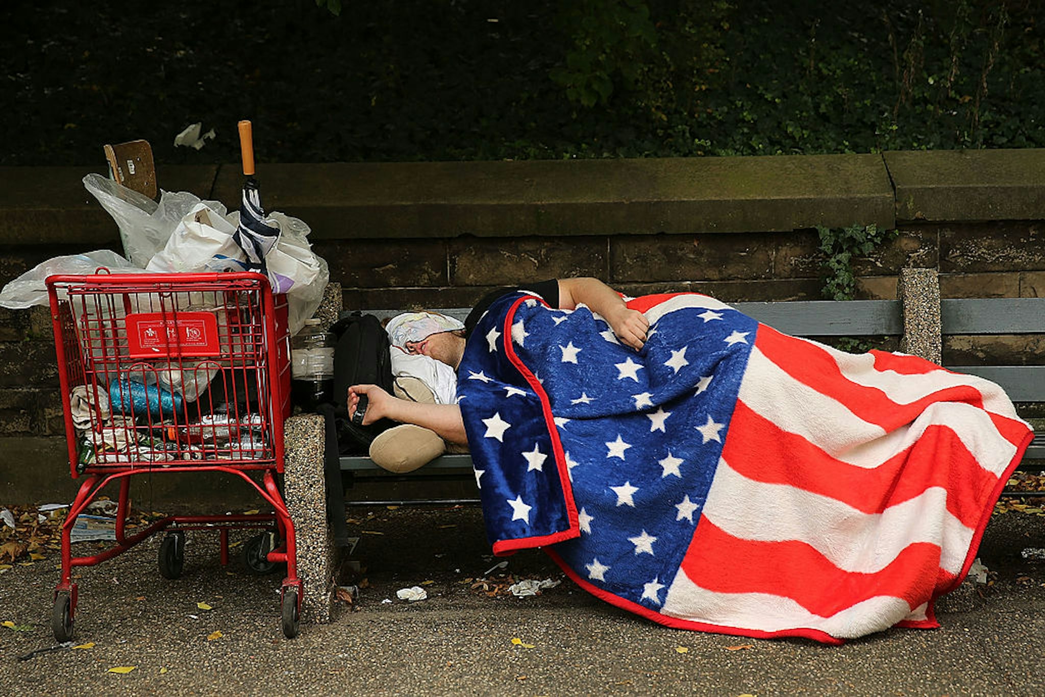 NEW YORK, NY - SEPTEMBER 10: A homeless man sleeps under an American Flag blanket on a park bench on September 10, 2013 in the Brooklyn borough of New York City. As of June 2013, there were an all-time record of 50,900 homeless people, including 12,100 homeless families with 21,300 homeless children homeless in New York City. (Photo by Spencer Platt/Getty Images)