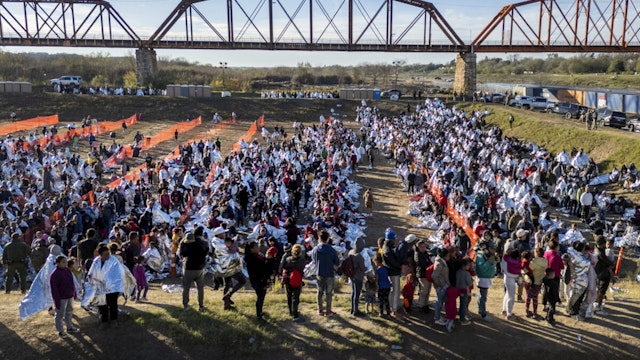 EAGLE PASS, TEXAS - DECEMBER 19: In an aerial view, thousands of immigrants, most wearing thermal blankets, await processing at a U.S. Border Patrol transit center on December 19, 2023 in Eagle Pass, Texas. Major surges of migrants illegally crossing the Rio Grande have overwhelmed U.S. border authorities in recent weeks.