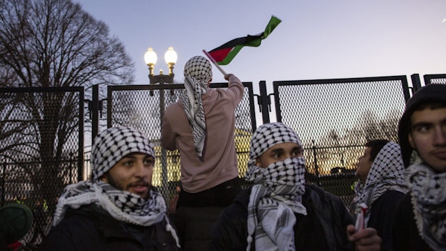 A demonstrator waves a Palestinian flag over the White House security fence while joining in a demonstration. the Pro-Palestinian demonstration in Washington DC.