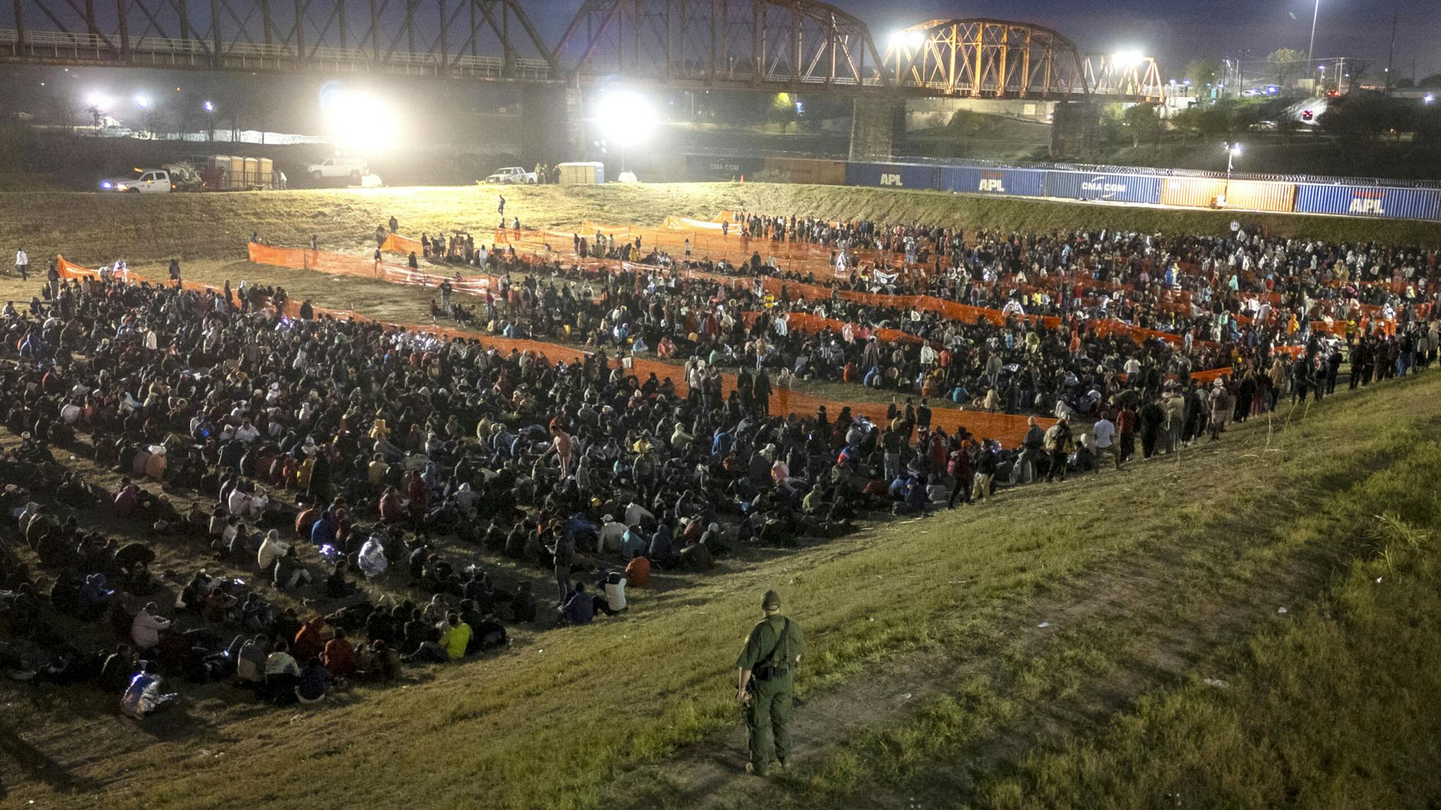 Surge Of Migrants Overwhelms Border Crossings EAGLE PASS, TEXAS - DECEMBER 18: A U.S. Border Patrol agent watches over more than 2,000 migrants at a field processing center on December 18, 2023 in Eagle Pass, Texas. A surge as many as 12,000 immigrants per day crossing the U.S. southern border has overwhelmed U.S. immigration authorities in recent weeks.