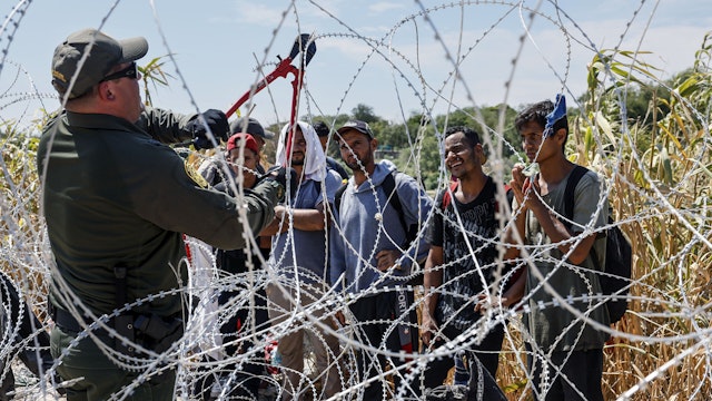 Eagle Pass, Texas, Sunday, September 24, 2023 - A border patrol agent cuts razor wire to allow migrants who've been waiting in the sun for hours, to come to a way station under the Camino Real International Bridge.