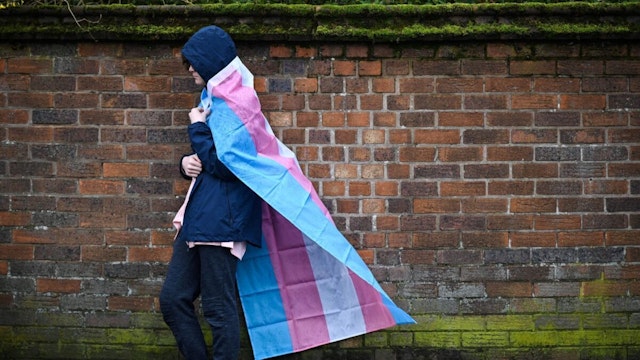 A mourner wrapped in the Transgender Flag waits for the horse-drawn carriage transporting the coffin of murdered transgender teenager Brianna Ghey, outside St Elphin's Church in Warrington, northern England on March 15, 2023, at the end of the funeral service.