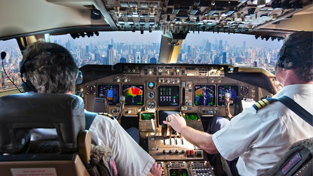 The cockpit of a modern passenger aircraft in flight. A view from the cockpit to the skyscrapers of the business center of a huge city. AlexeyPetrov. Getty Images.