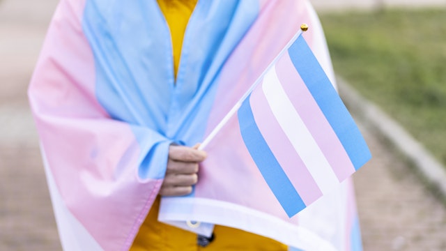 Transgender woman covered with the transgender flag and holding a flag in the hand for defending her rights