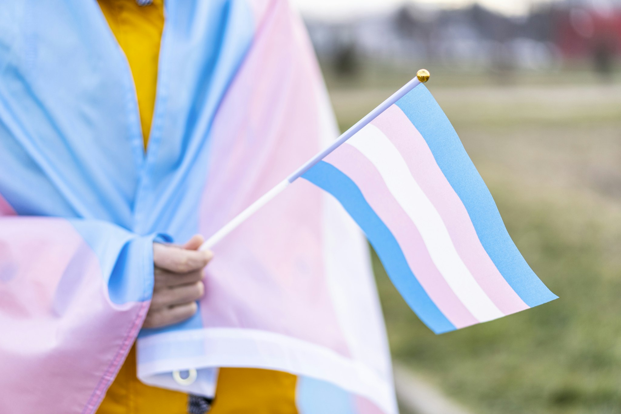 Transgender covered with the transgender flag and holding a flag in the hand for defending her rights