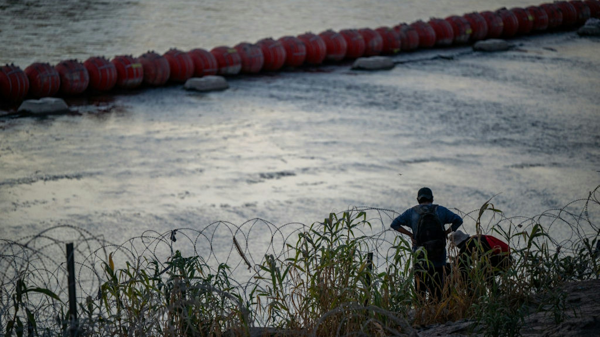 EAGLE PASS, TEXAS - SEPTEMBER 11: Migrants help each other through barbed-wire fencing after crossing the Rio Grande river near the buoy barriers on September 11, 2023 in Eagle Pass, Texas. The Court of Appeals have temporarily halted removal of the floating buoy barriers located in the river. The buoys have sparked controversy and tension amongst the United States and Mexico as claims of violating human rights have reached congress. The Department of Justice has filed a lawsuit against the state of Texas as Gov. Greg Abbott has vowed “to take this fight all the way to the U.S. Supreme Court.”