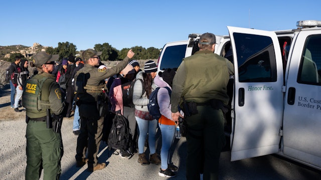 SAN DIEGO, CALIFORNIA - FEBRUARY 13: Migrants board a U.S. Border Patrol patrol vehicle on February 13, 2024 in San Diego, California.
