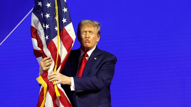 NATIONAL HARBOR, MARYLAND - FEBRUARY 24: Republican presidential candidate and former U.S. President Donald Trump hugs an American flag as he arrives at the Conservative Political Action Conference (CPAC) at the Gaylord National Resort Hotel And Convention Center on February 24, 2024 in National Harbor, Maryland. Attendees descended upon the hotel outside of Washington DC to participate in the four-day annual conference and hear from conservative speakers from around the world who range from journalists, U.S. lawmakers, international leaders and businessmen. (Photo by Anna Moneymaker/Getty Images)