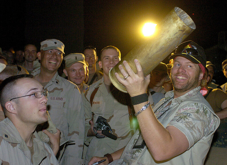 KABUL, AFGHANISTAN - JUNE 3: In this handout image provided by the United Service Organizations (USO), country music star Toby Keith (R) holds an artillery shell he is asked to autograph by U.S. troops at Camp Phoenix after a USO performance for coalition forces June 3, 2004 in Kabul, Afghanistan. Keith, who swept top honors at last week's Academy of Country Music Awards, is touring U.S. military installations for the USO in Kosovo, Germany, Italy and the Persian Gulf. (Photo by Mike Theiler/USO via Getty Images)