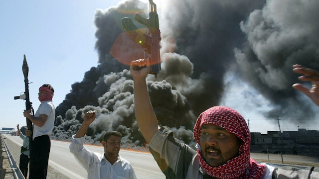 Iraqi Sunni Muslim insurgents celebrate in front of a burning US convoy they have attacked earlier 08 April 2004 in Abu Gharib, on the outskirts of the flashpoint town of Fallujah.