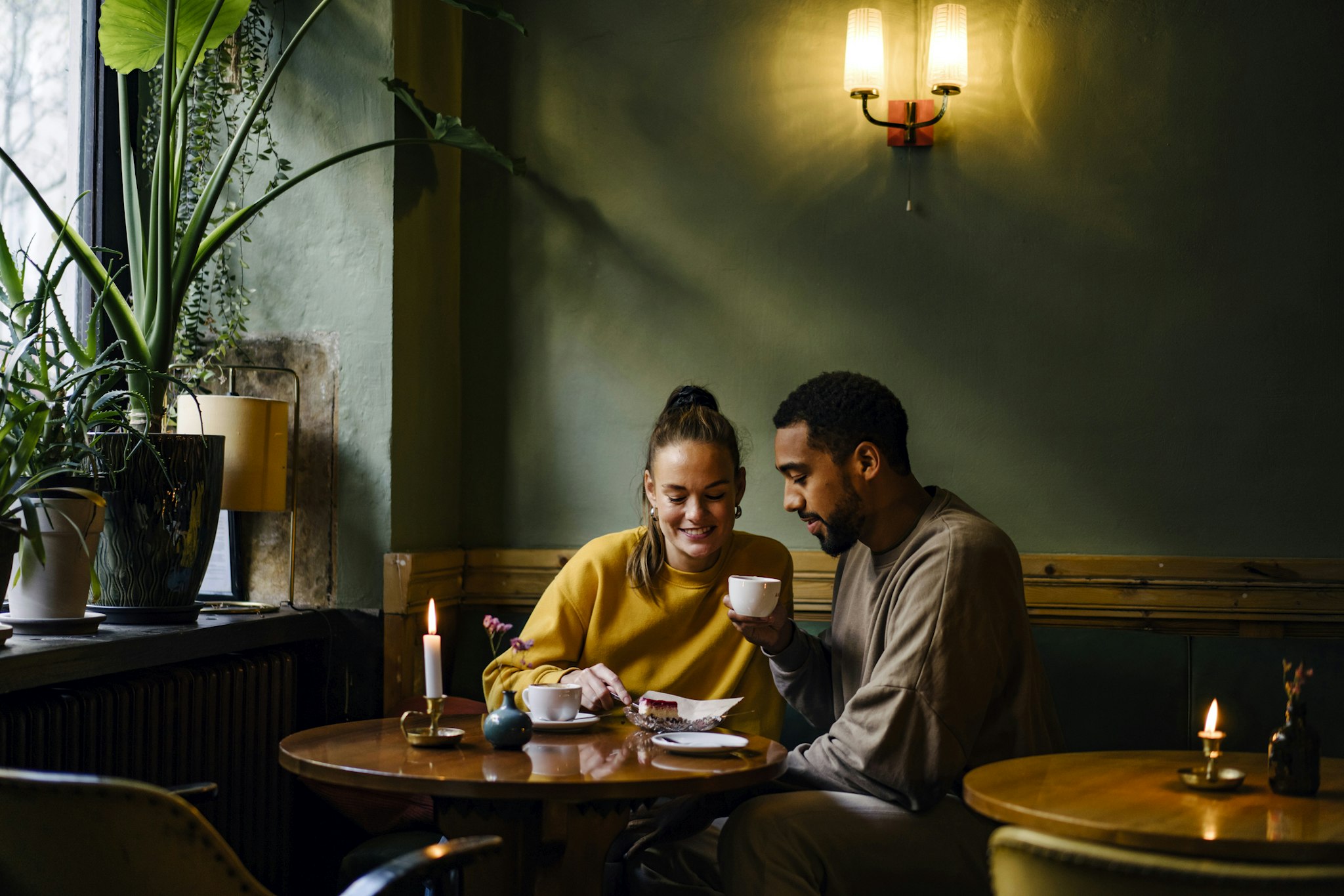 Janina Steinmetz. Getty Images. Wide shot with copy space of couple having cappuccinos and cheesecake in coffee shop.