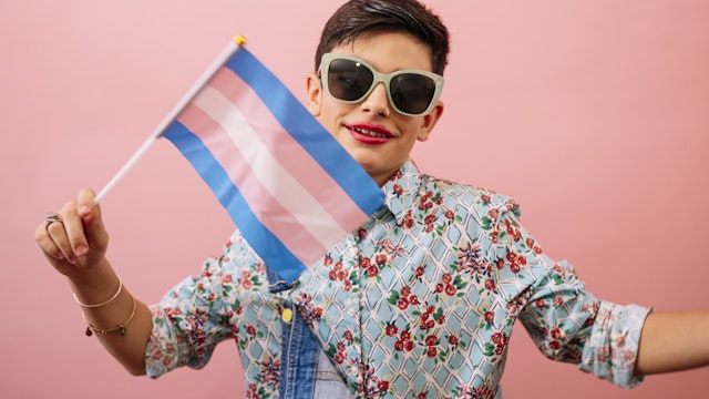 Young boy feeling girly and holding a trans flag. Gender confusion in adolescence.