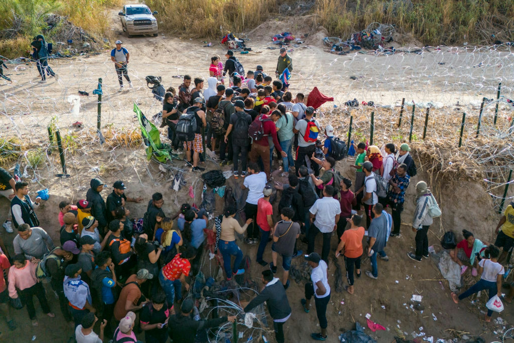 EAGLE PASS, TEXAS - SEPTEMBER 30: As seen from an aerial view, a U.S. Border Patrol agent supervises as immigrants walk into the United States after crossing the Rio Grande from Mexico on September 30, 2023 in Eagle Pass, Texas. The agent had cut coils of razor wire to let them pass through for processing. Immigration and border security have become major issues in ongoing negotiations to fund the U.S. government. A recent surge in immigrant crossings has overwhelmed border authorities.