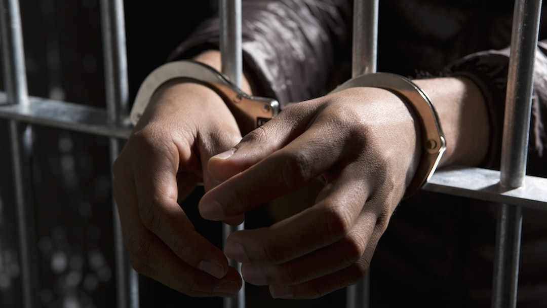 A prisoner behind bars with hands cuffed -- Caspar Benson via Getty Images