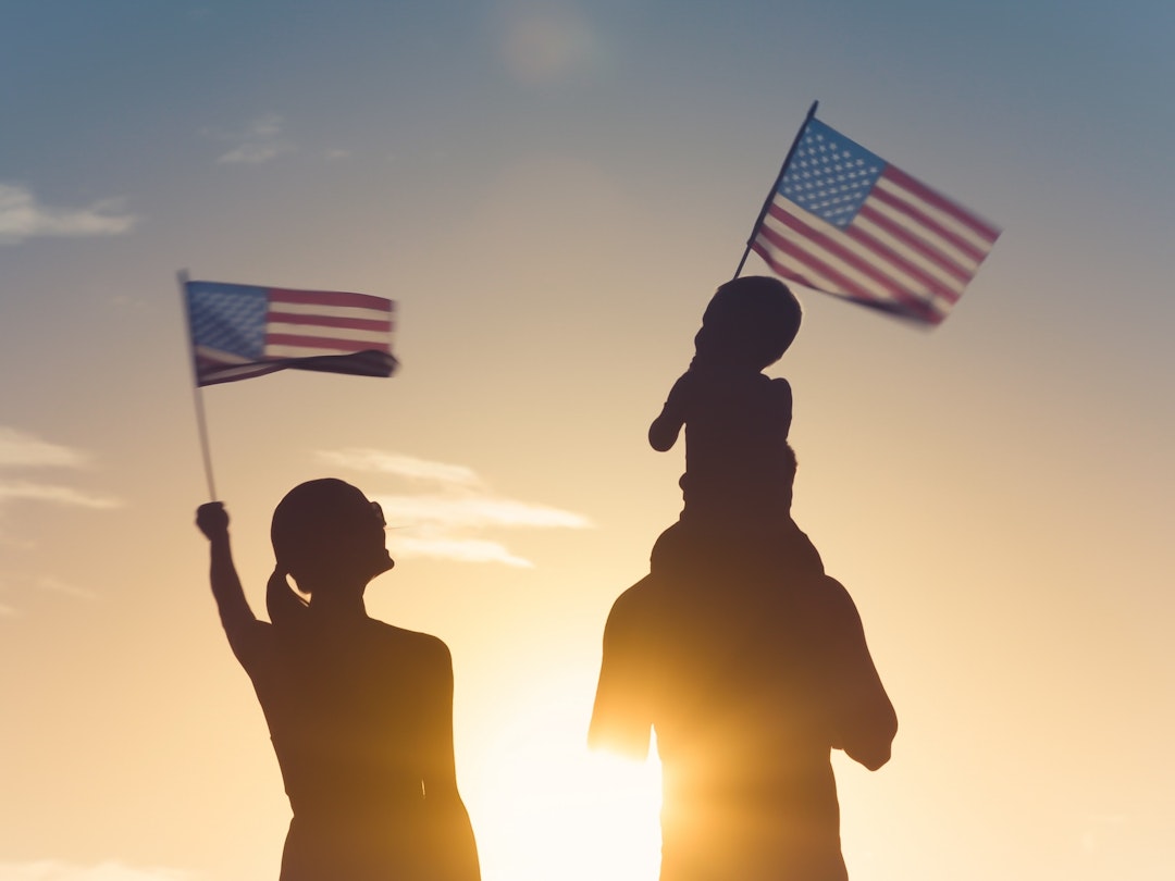 kieferpix. Getty Images. Patriotic silhouette of family waving American USA flags.