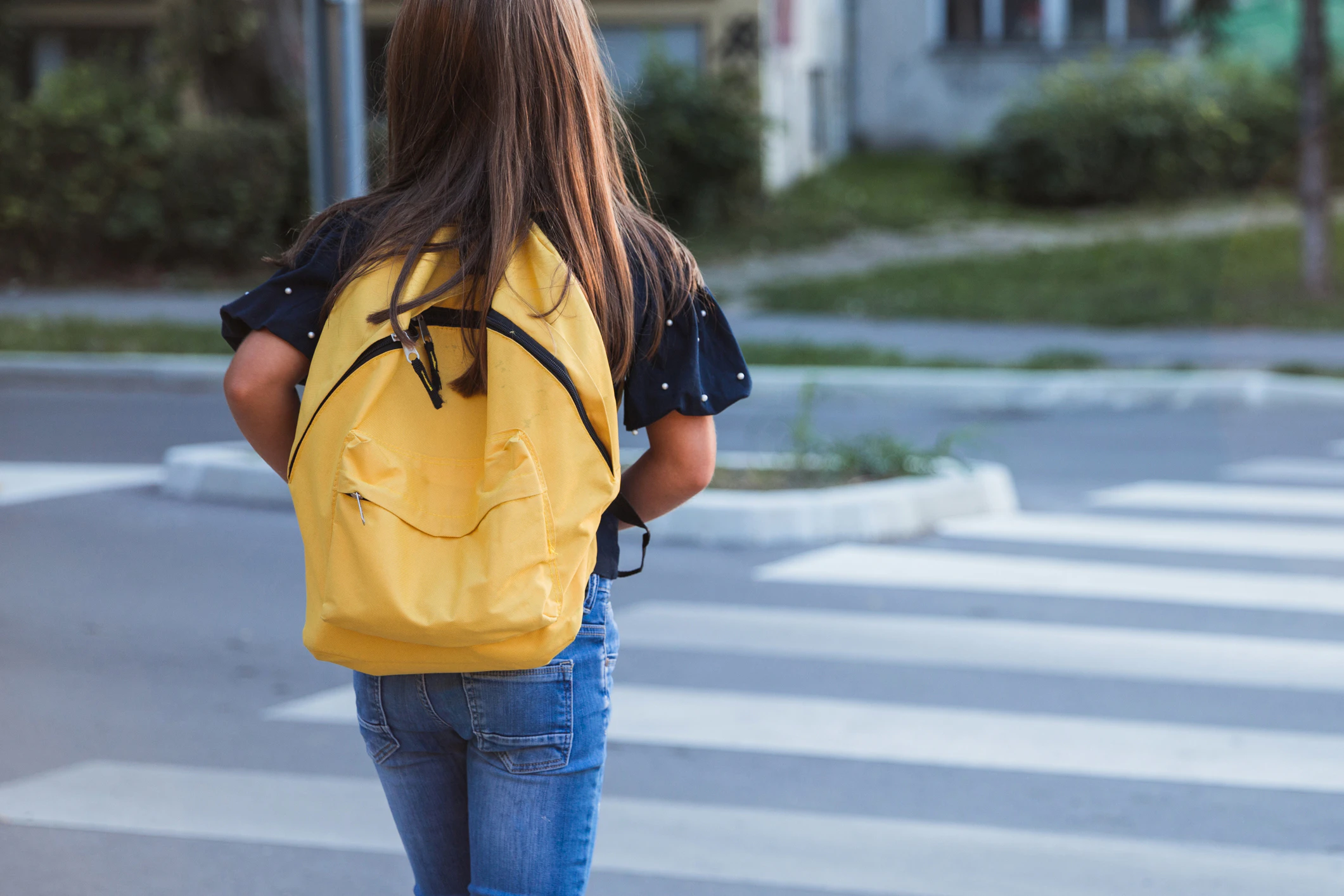 Kid wearing yellow school bag when crossing the street on her way to school