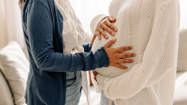 JLco - Julia. Getty Images. Amaral Unrecognizable young woman touching a surrogate mother's belly bump. Young woman spending time with her surrogate at home. Woman feeling the movement of a pregnant woman's baby.