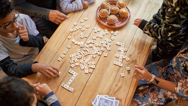 High angle view family playing scrabble at dining table with muffins