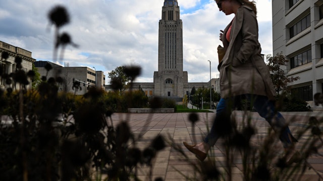 A pedestrian walks through Capitol Park as the Nebraska State Capitol is seen in the background on Wednesday, October 26, 2023 in Lincoln, Nebraska.